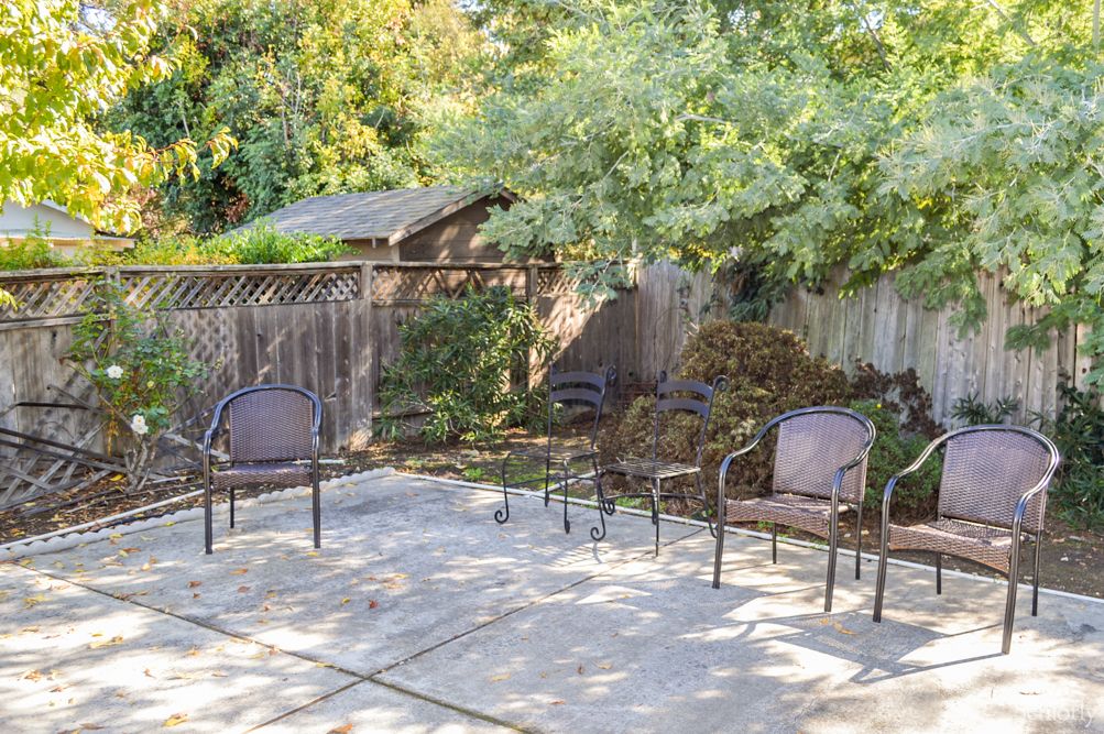 A peaceful backyard patio with outdoor chairs surrounded by trees and a wooden fence.