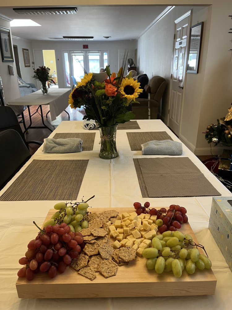 A dining table set with placemats, a vase of sunflowers, and a cheese platter with grapes and crackers.
