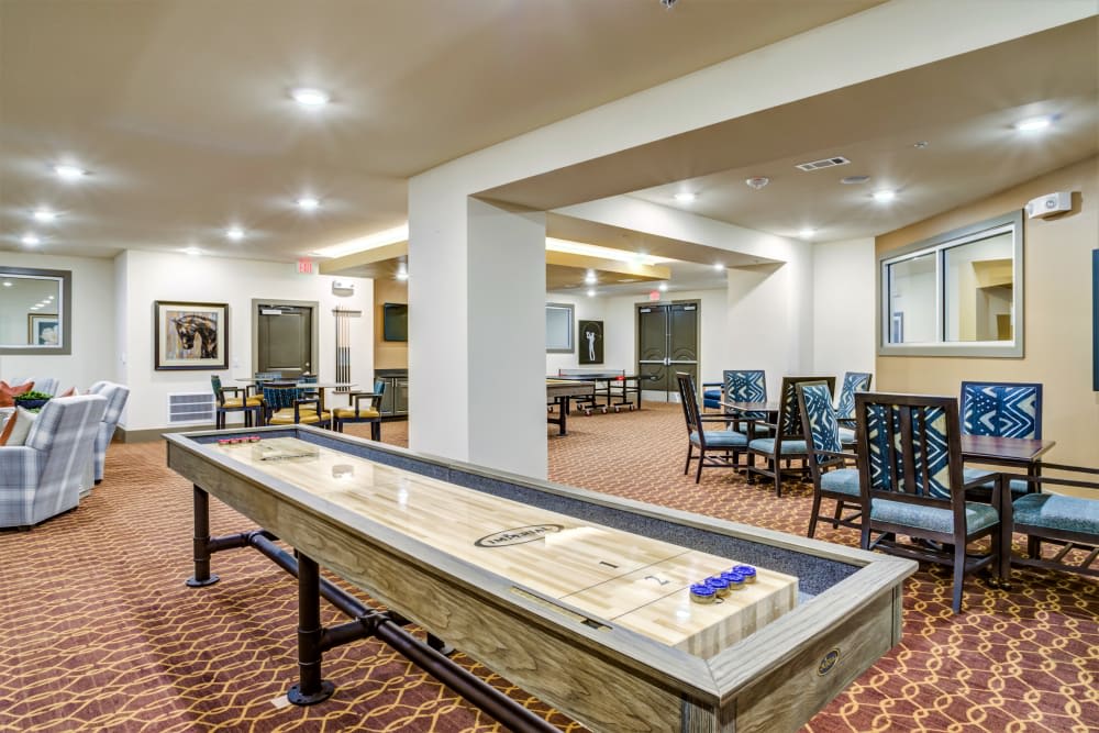 A well-lit game room featuring a shuffleboard table and seating area.