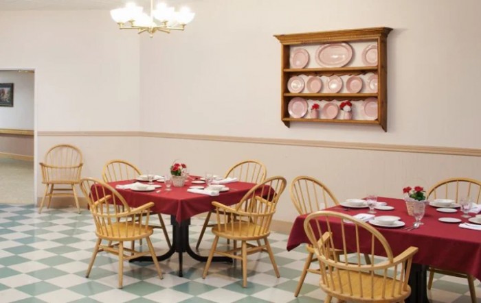 A cozy dining area with tables set for a meal, featuring red tablecloths and wooden chairs.
