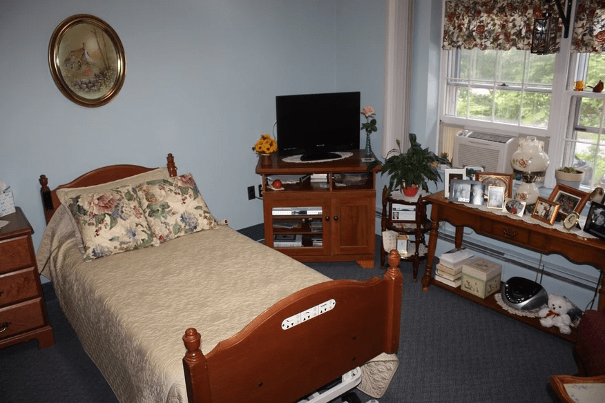 A cozy bedroom with a bed, television stand, potted plant, and window.