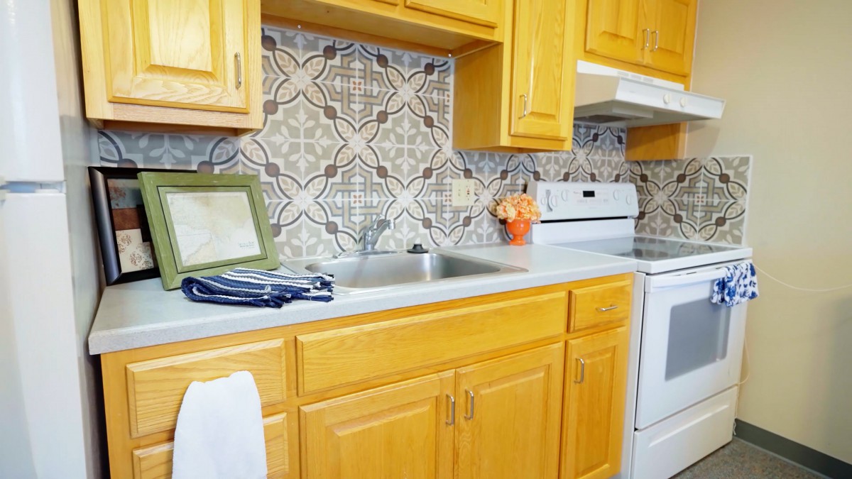 A bright kitchen with wooden cabinets, a patterned tile backsplash, and modern appliances.