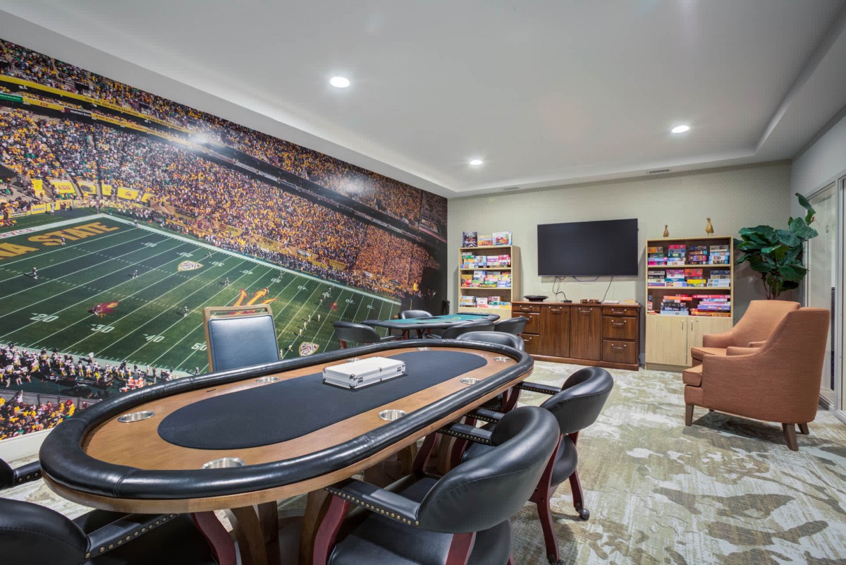 A sports-themed game room featuring a poker table and chairs, with a large mural on the wall and a television.