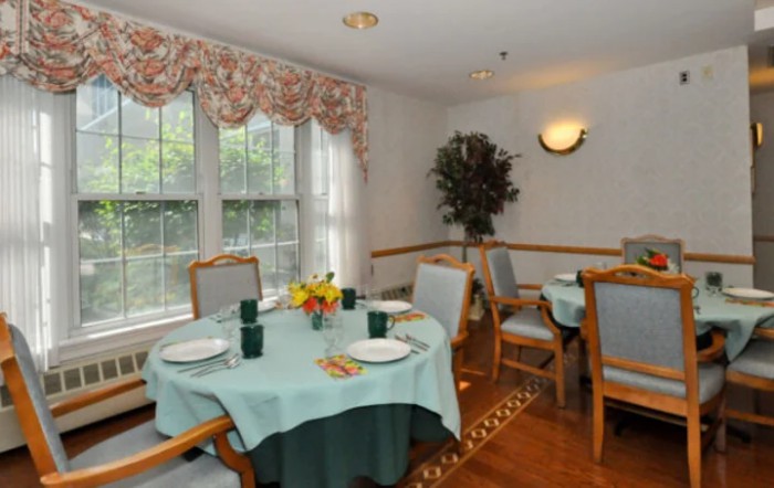 A cozy dining room with elegantly set tables and large windows allowing natural light to fill the space.