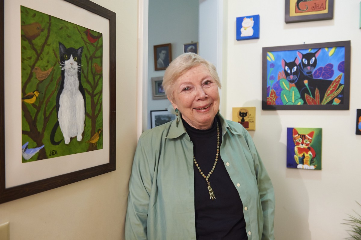 A woman stands in an art-filled room with various cat paintings on the walls.