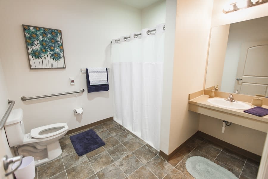 An accessible bathroom featuring a shower with a curtain, toilet, sink, and tiled floor.
