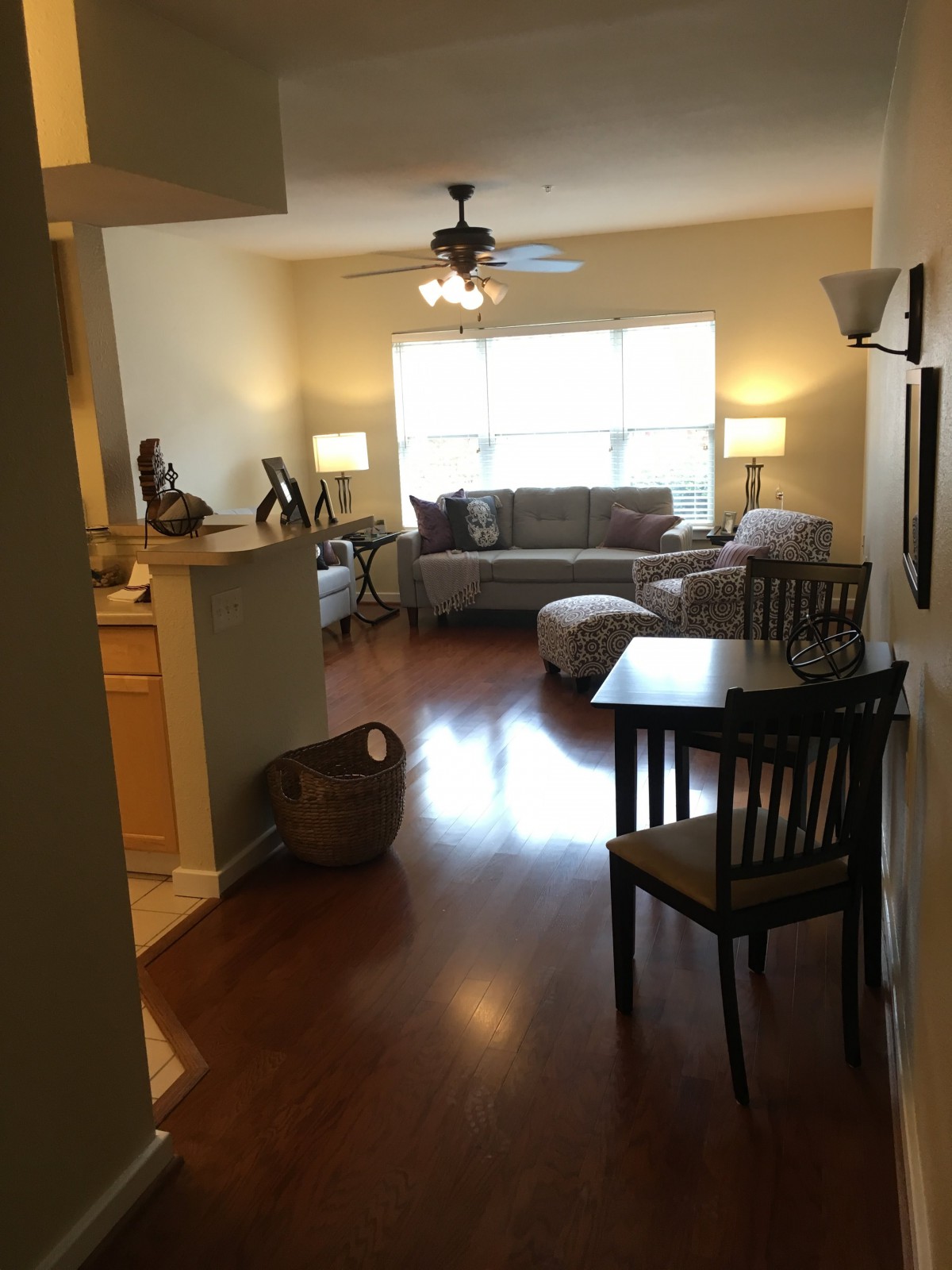 A cozy living room with wood flooring, featuring a sofa, chairs, and ample natural light.
