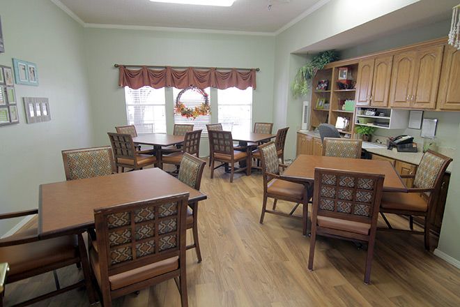 A cozy dining area with wooden tables and chairs, decorated with curtains and plants.