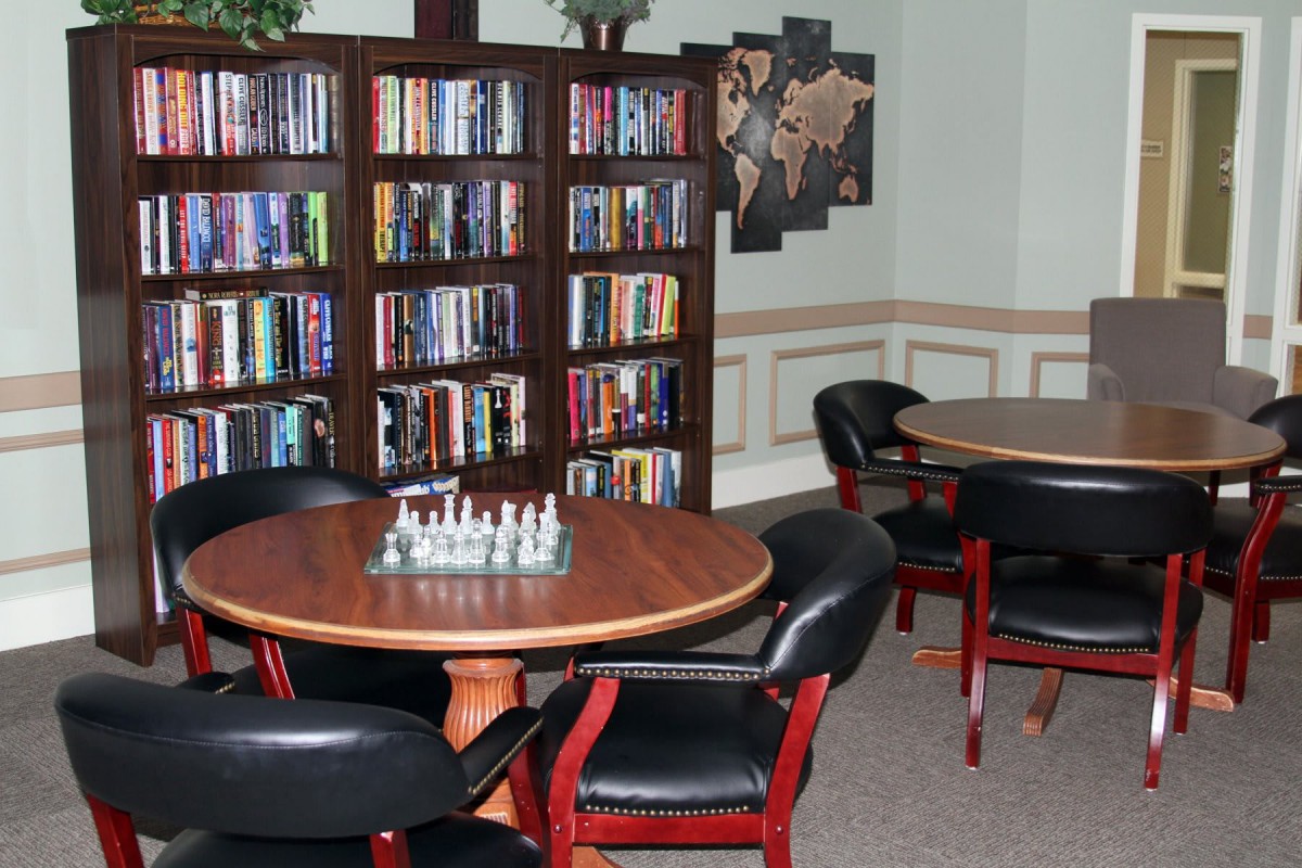 A cozy library corner with bookshelves and a chess board on a round table.