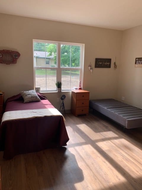 A simple and minimalist bedroom with two beds bathed in sunlight from a large window.