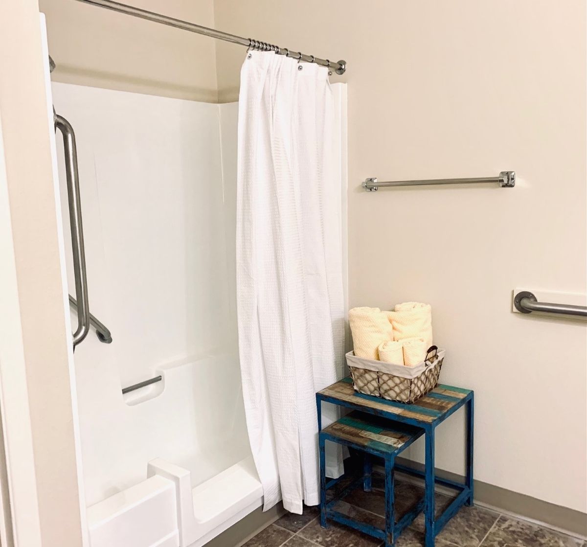 A clean and simple bathroom with a shower, white curtain, and organized towels on a blue shelf.