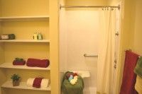 A neatly arranged bathroom with a shower and colorful towels on shelves.