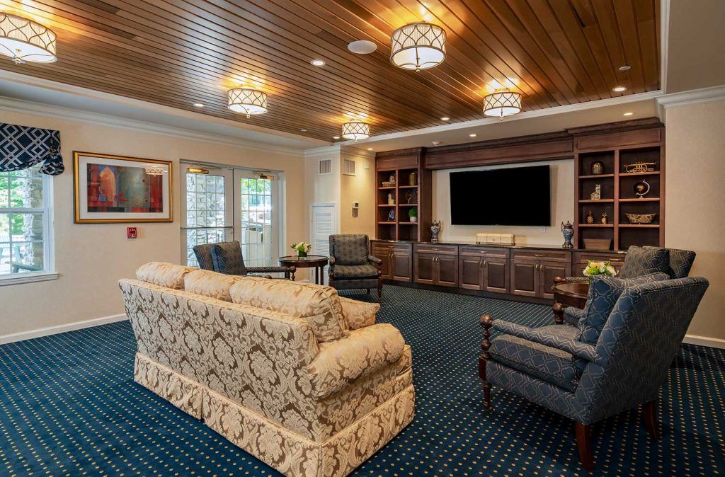 A cozy living room featuring elegant furniture, a large television, and wooden ceiling details.