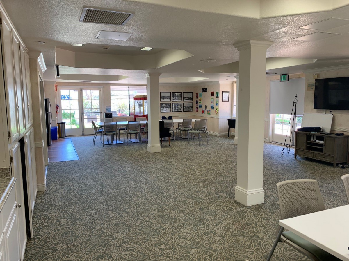 Spacious community area with tables and chairs, well-lit with natural light from large windows.
