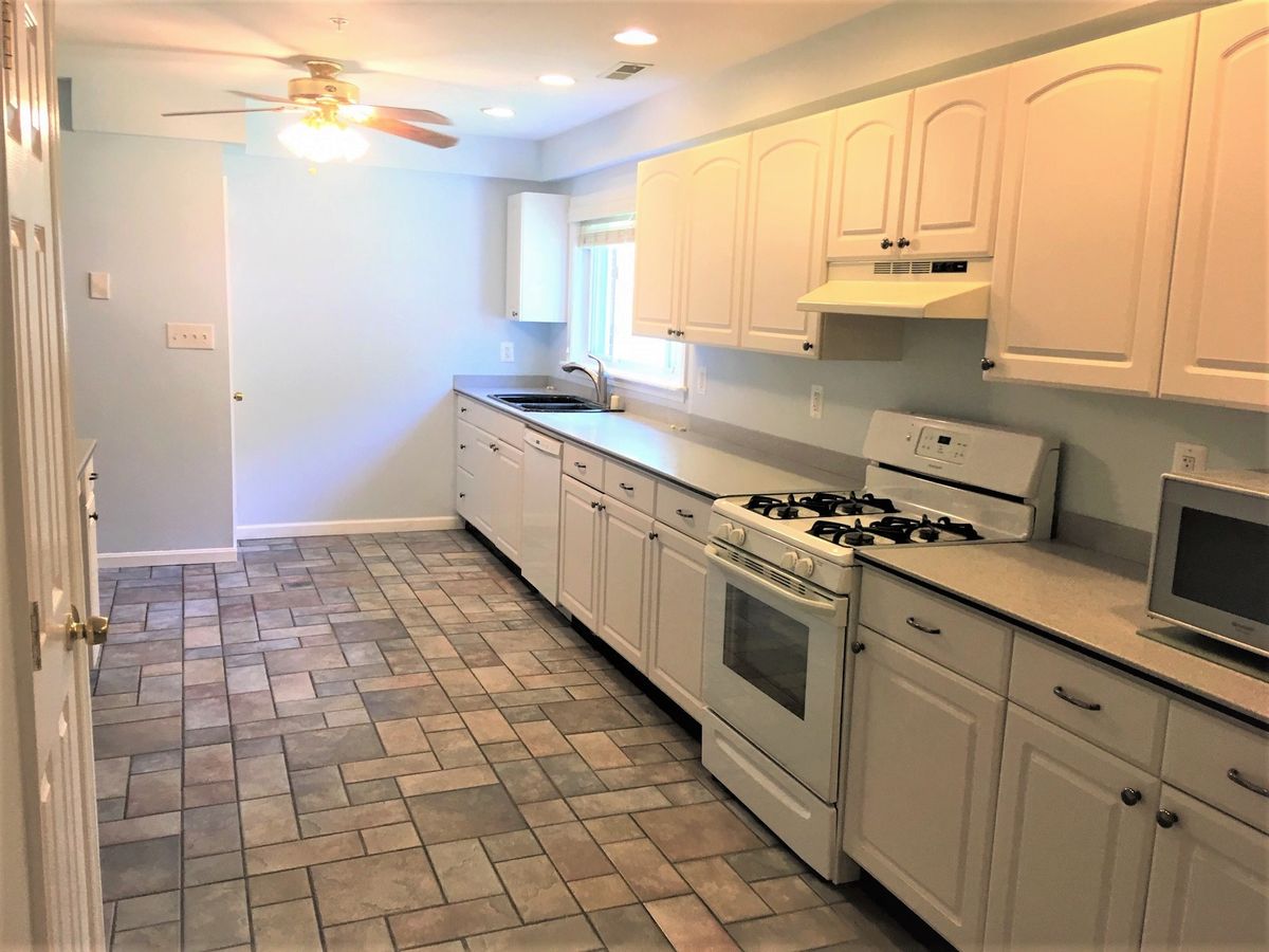 A spacious kitchen with white cabinetry, a gas stove, and tiled flooring.
