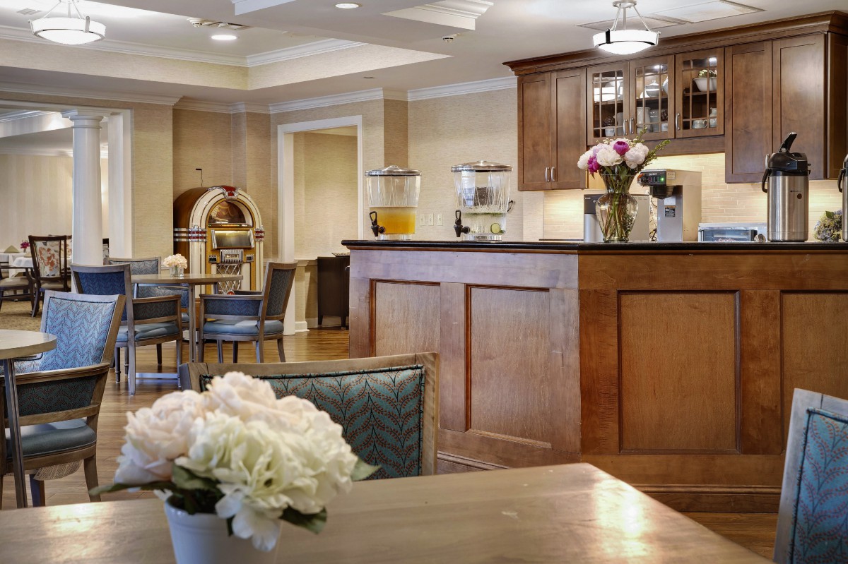 A cozy kitchen area featuring a wooden bar counter with flowers and coffee-making equipment.