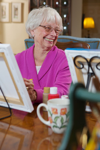 An elderly woman joyfully engaged in a painting activity, surrounded by art supplies.