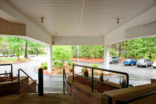 A view from under a covered area, looking towards a parking lot surrounded by greenery.