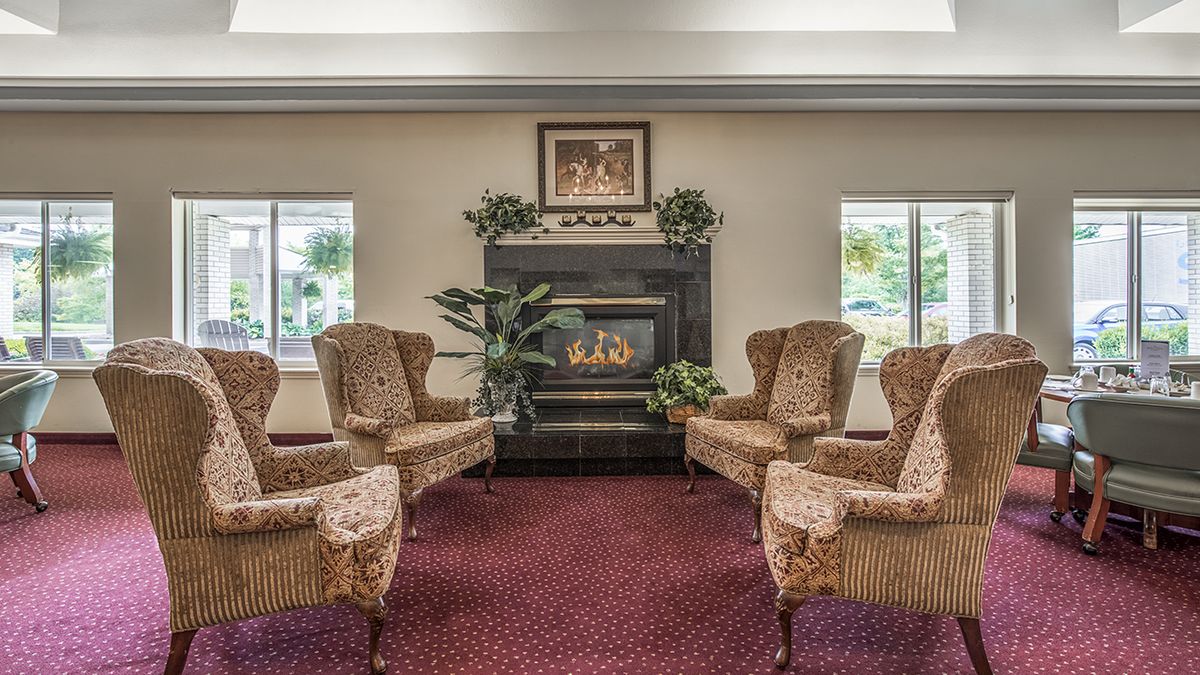 A cozy living room with a fireplace, surrounded by comfortable chairs and decorated with artwork and plants.
