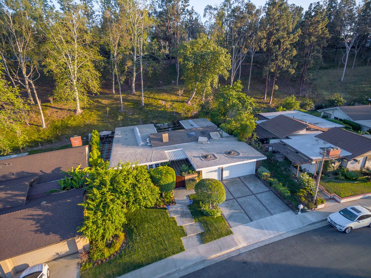A modern house in a suburban neighborhood surrounded by trees, captured from an aerial perspective.