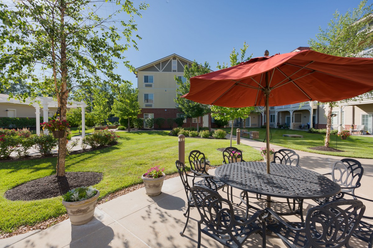 A peaceful garden patio with outdoor seating and a large umbrella on a sunny day.