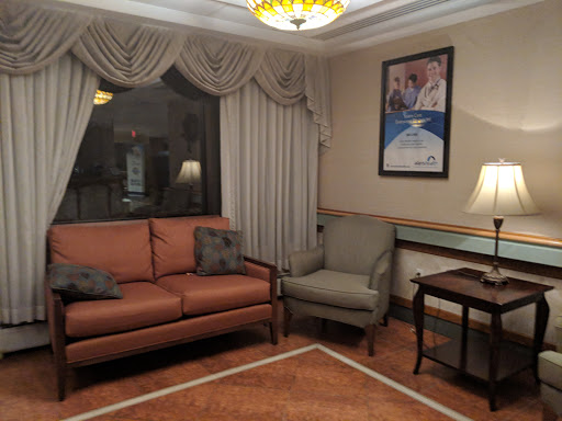 A cozy living room setup featuring a reddish-brown sofa, an armchair, a side table with a lamp, and elegant curtains.