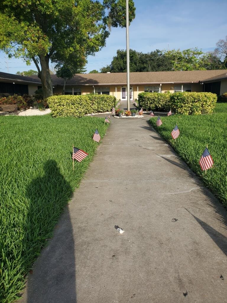 A pathway lined with small flags leads to a house, bordered by neatly trimmed grass.