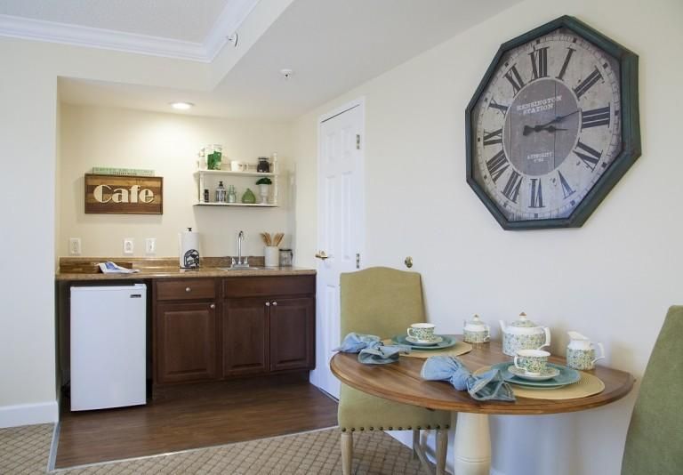 A cozy kitchen and dining area with a large wall clock and table set for two.