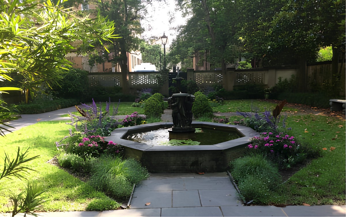 A serene garden with a central fountain surrounded by lush greenery and flowers.