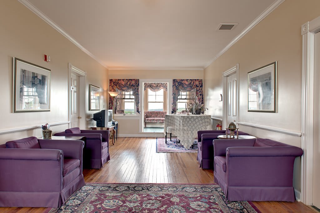 A traditional living room with purple chairs and a wooden floor, featuring a decorative rug and large windows.