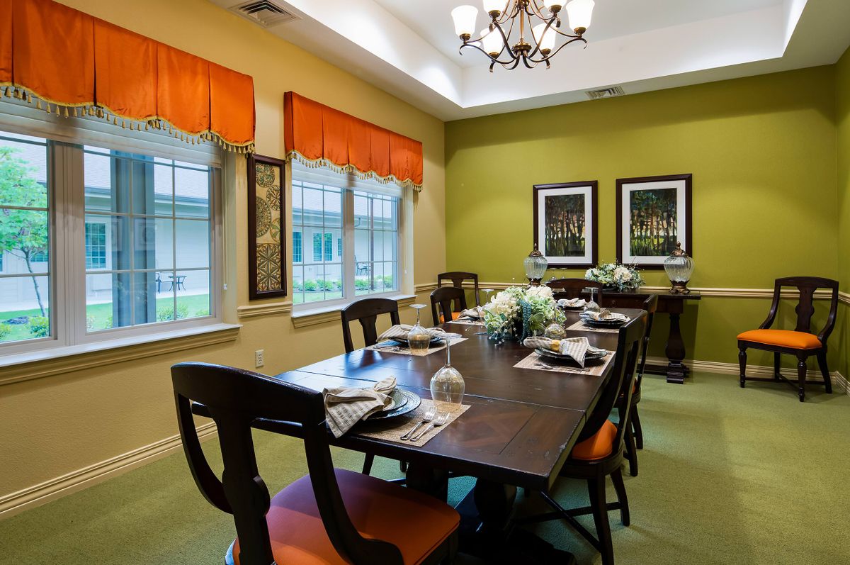 A well-decorated dining room with a long table and chairs, featuring vibrant curtains and elegant lighting.