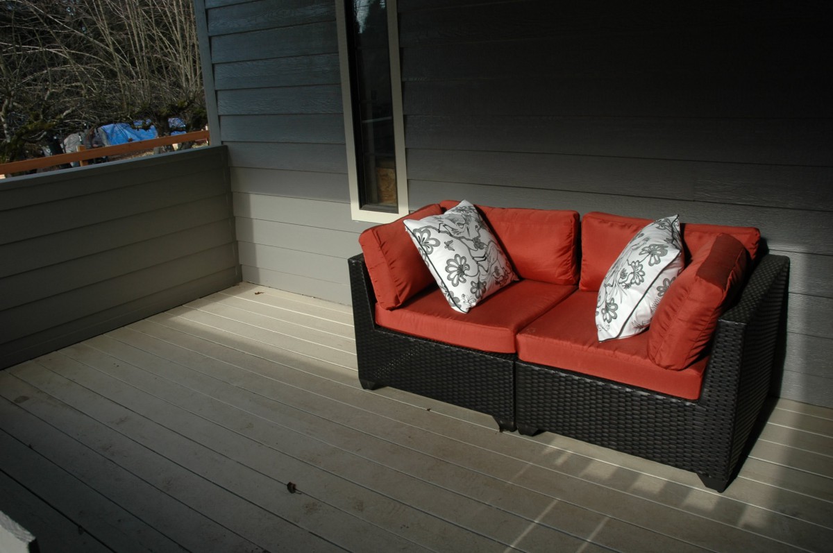 A cozy outdoor patio with a wicker sofa adorned with red cushions and decorative pillows.