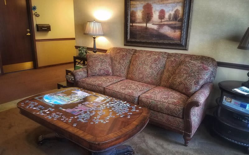 A cozy living room setup with a patterned couch, coffee table with a puzzle in progress, and warm lighting.