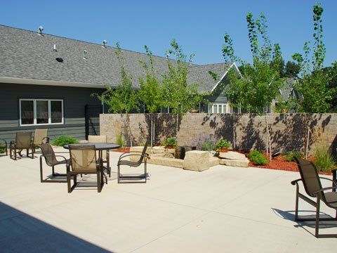 A spacious patio area with outdoor furniture, surrounded by a garden and young trees.