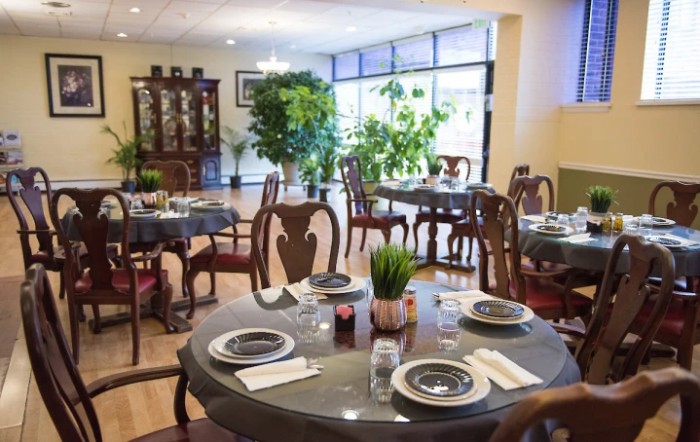 A cozy restaurant dining area with elegantly set tables and lush plants by the window.