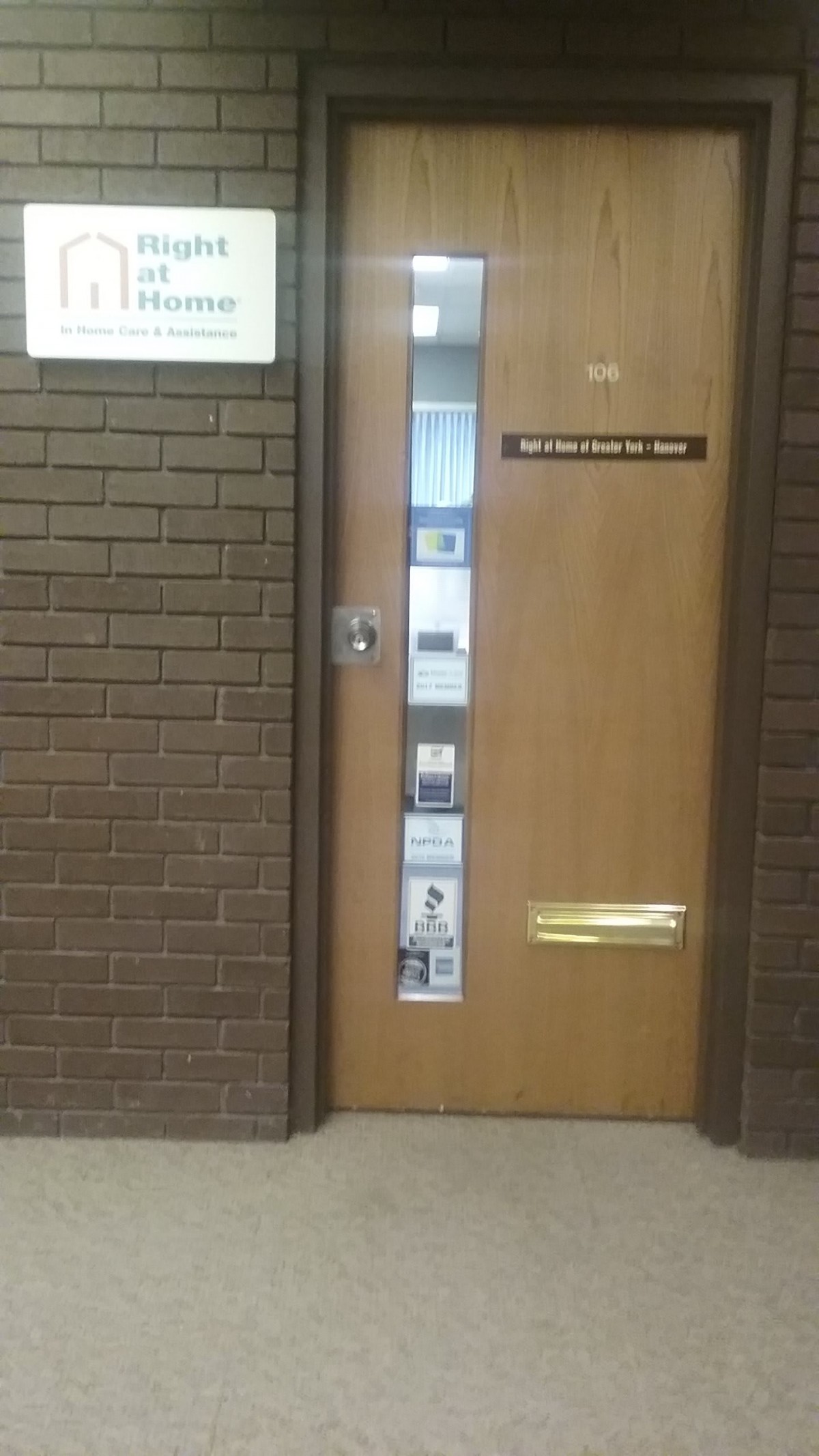A wooden office door with a vertical window and signs, set in a brick wall.