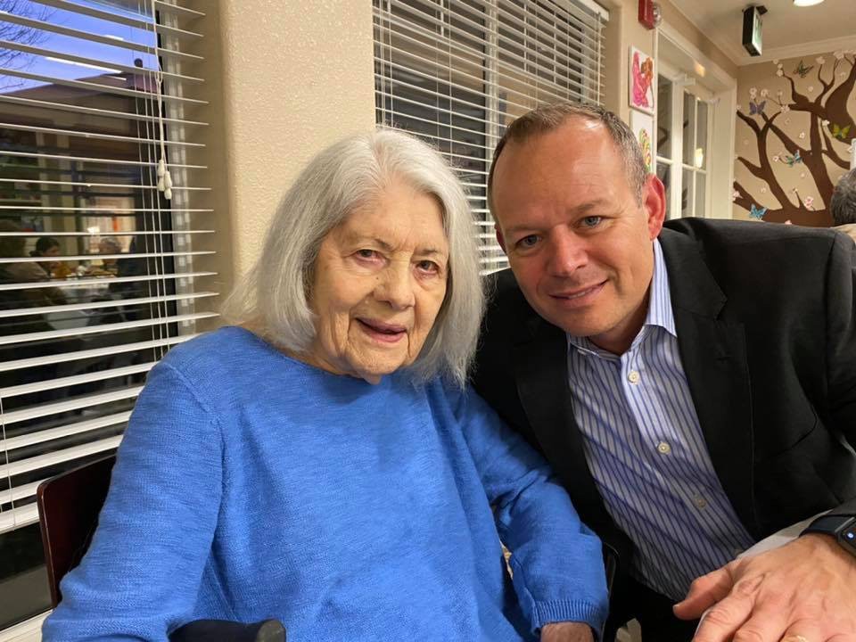An elderly woman and a man smiling together indoors.