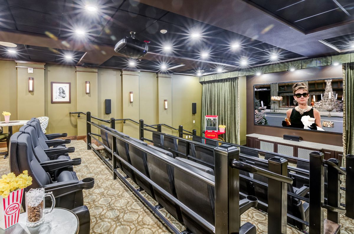 A luxurious home theater setup featuring tiered seating, a large projector screen, and modern lighting.