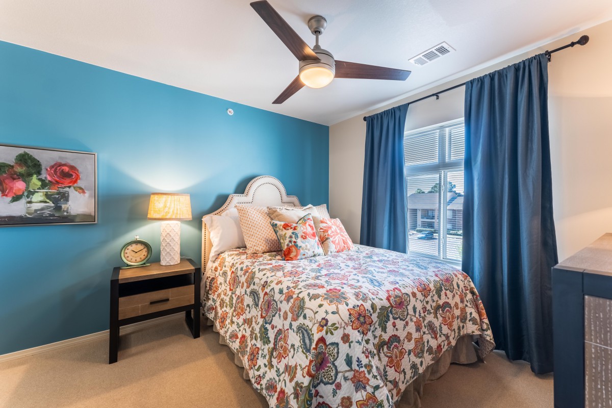 A cozy bedroom featuring floral bedding, blue accent wall, and natural light streaming through the window.