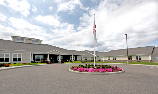A welcoming entrance to a modern facility, surrounded by vibrant flowers and an American flag.
