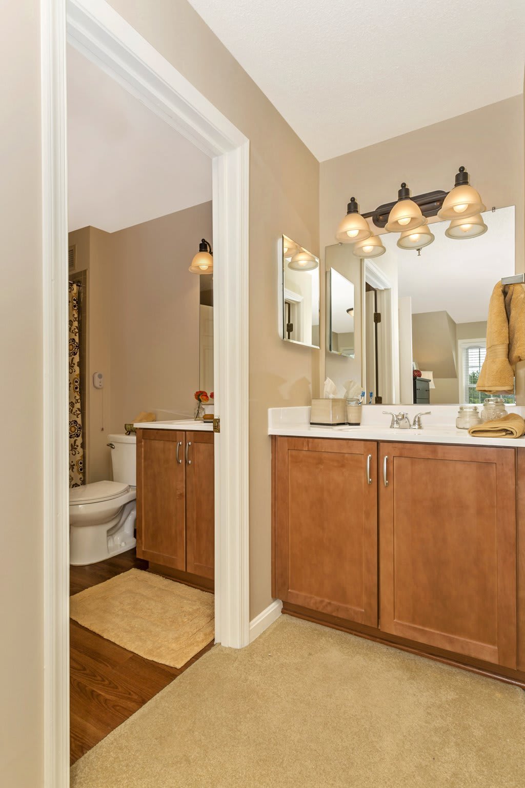 A bathroom with a wooden vanity, mirror, and lighting fixtures, featuring a sink and adjacent toilet.