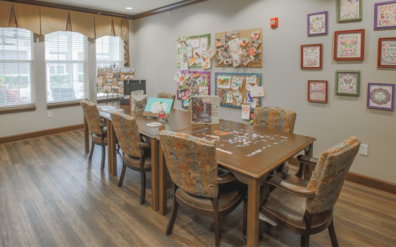 A cozy room with a large table surrounded by chairs, adorned with artwork and puzzles.