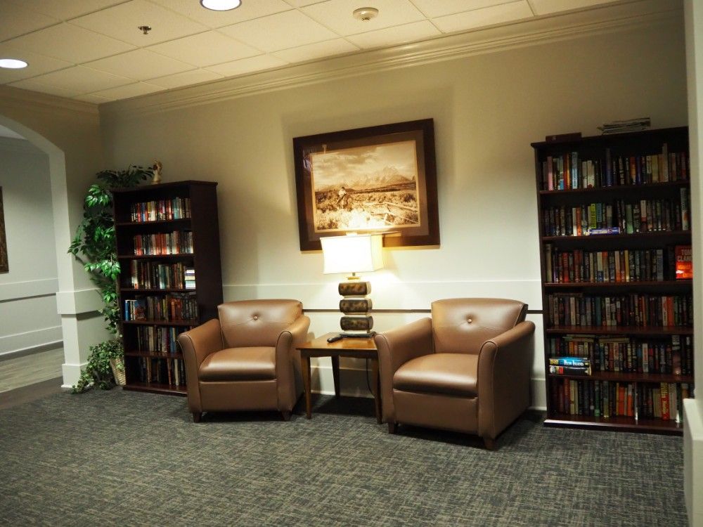 A cozy reading area with leather chairs, bookshelves, and a lamp.