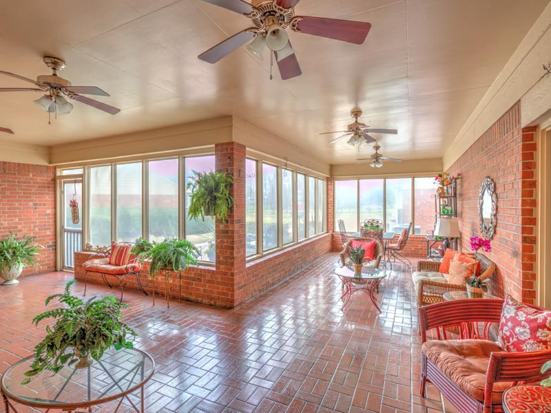 A spacious sunroom filled with natural light, featuring brick walls, cozy furniture, and an array of potted plants.