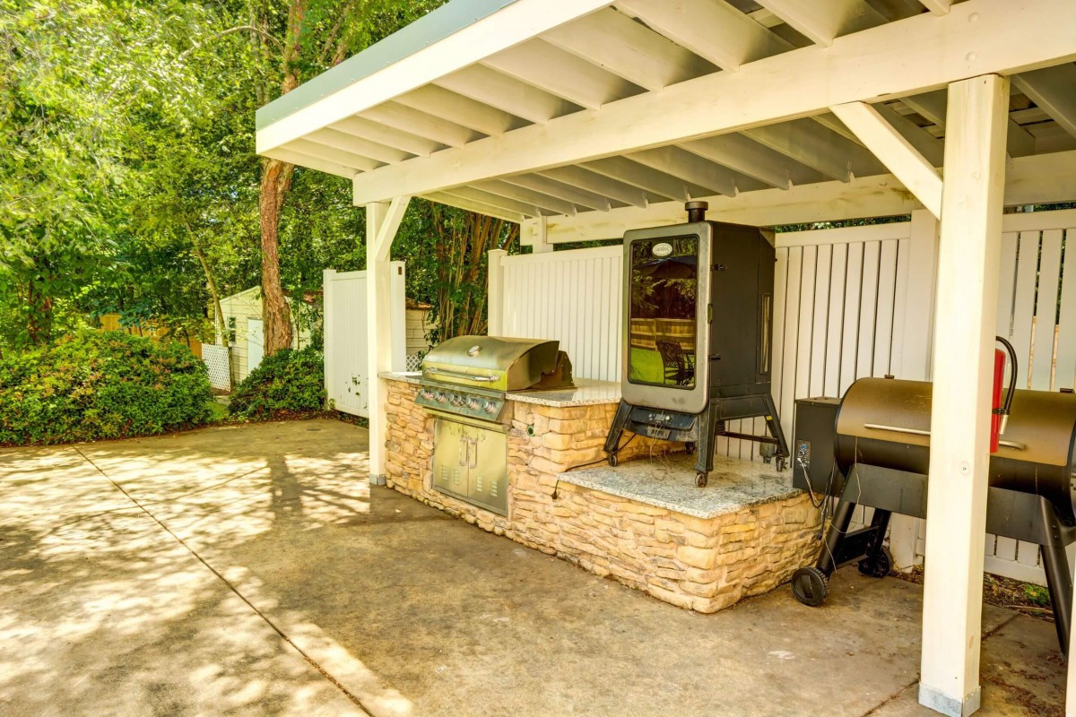 A covered outdoor kitchen area featuring a barbecue grill and smoker on a patio.