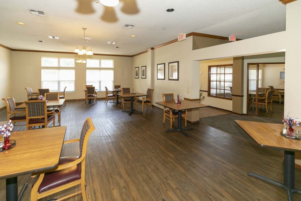 A spacious dining area with wooden floors and several tables and chairs arranged near large windows.