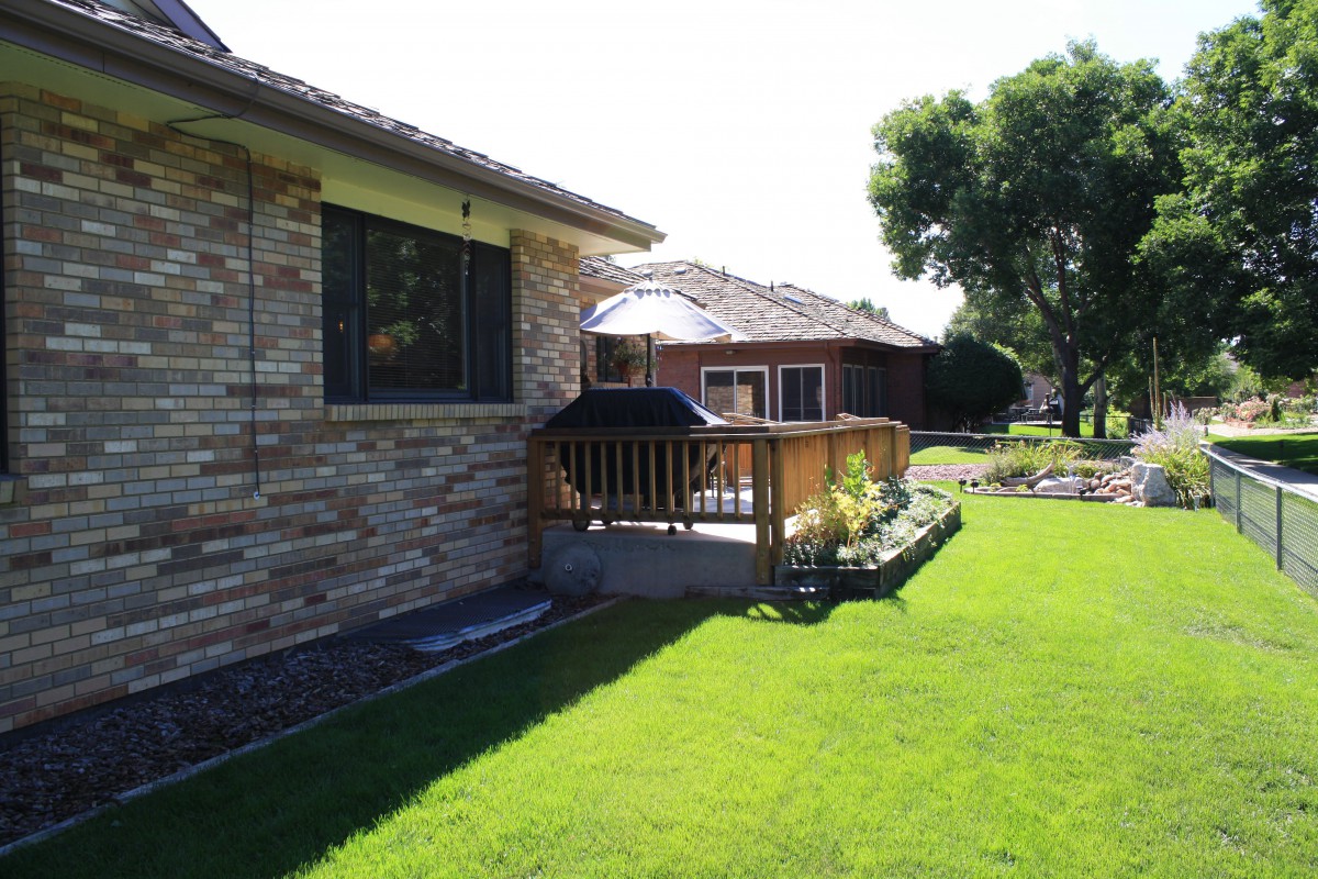 A sunny day view of a house with a lush green lawn and a wooden deck in the backyard.