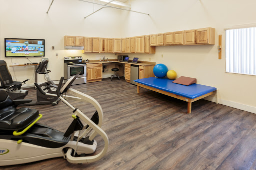 A well-equipped gym area featuring exercise machines, therapy balls, and a padded workout surface.