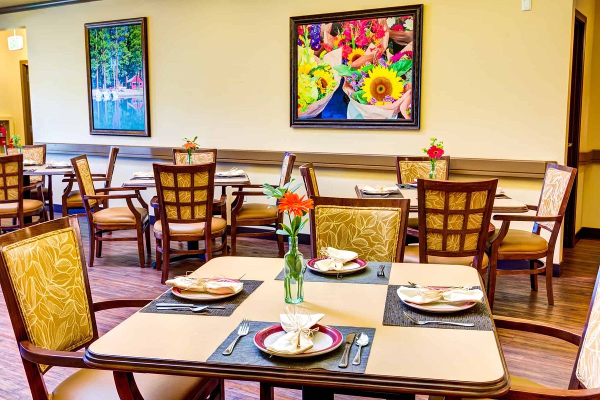 A brightly lit dining area with neatly arranged tables and chairs, adorned with colorful floral artwork on the walls.