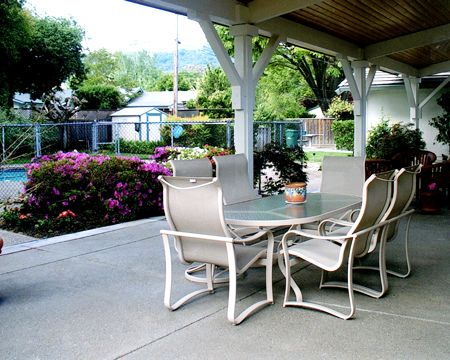 A covered patio with outdoor furniture surrounded by a garden.
